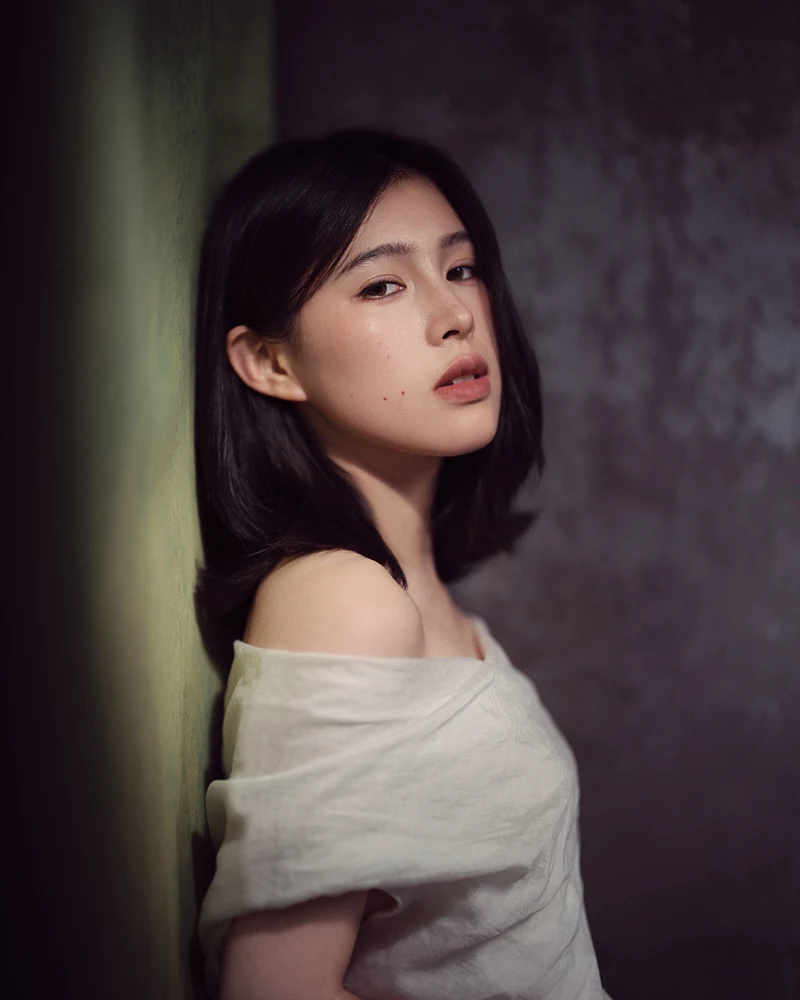Stunning black and white portrait photography of a woman with her hair up, looking subtly over her shoulder in an open embroidered white shirt.