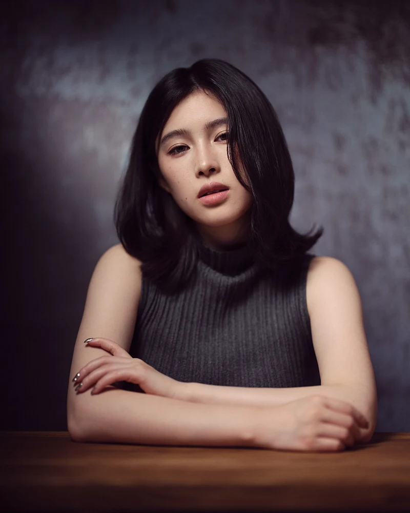 Creative studio portrait featuring a woman looking through a subtly blurred foreground element, adding a dreamy depth to the composition.